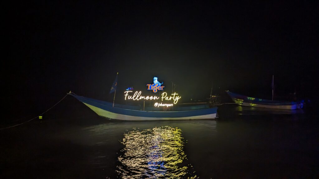 boat floating in ocean at the phangan full moon party with light up sign saying Full monn party phangan